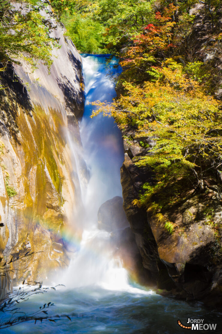 Mesmerizing autumn waterfall in Shosenkyo Valley, Japan amidst vibrant foliage and lush greenery.