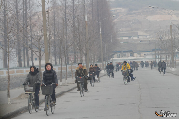 Winter street scene in Pyongyang, North Korea: people walking and riding bicycles in the cold.