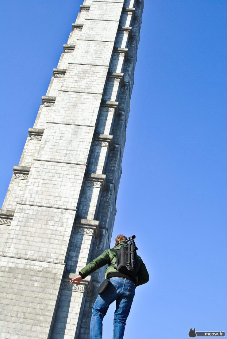 Urban climber scaling tall concrete skyscraper under clear blue sky, showcasing challenge and scale.