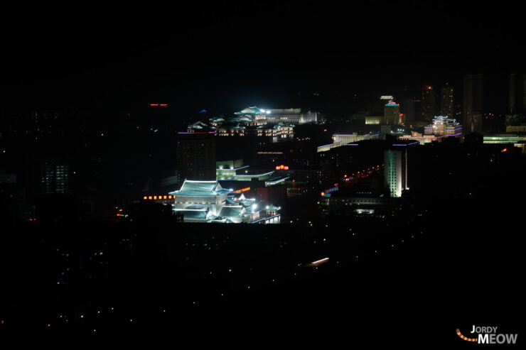 Nighttime skyline of vibrant Pyongyang, North Korea with illuminated buildings and central government structure.