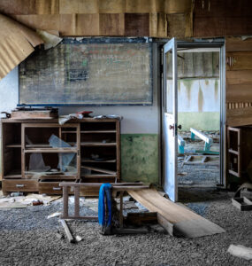 Abandoned classroom on Gunkanjima Island: decaying furniture, haunting atmosphere of forgotten mining community.