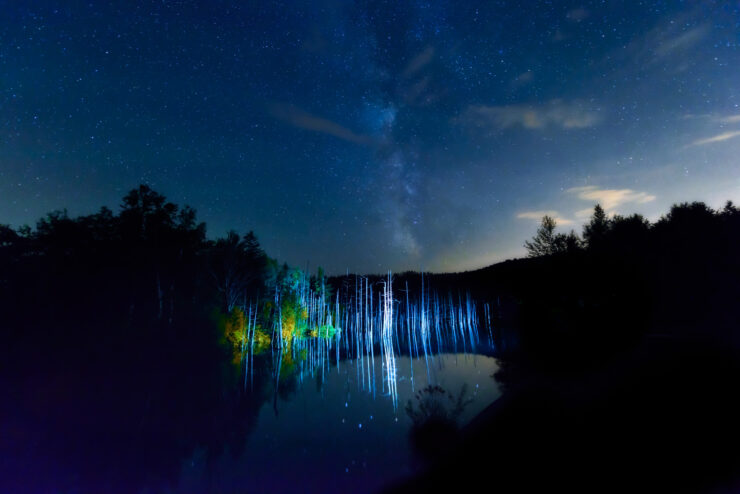 Mystical night scene at Blue Pond in Biei, Hokkaido, with colorful celestial lights.