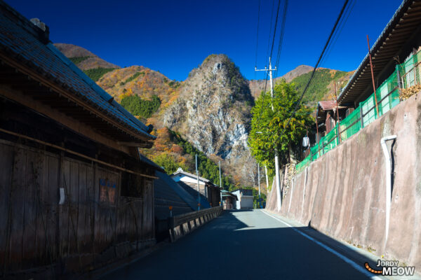 Serene autumn landscape with Inamura Rock, traditional Japanese buildings, lush greenery, and clear sky.